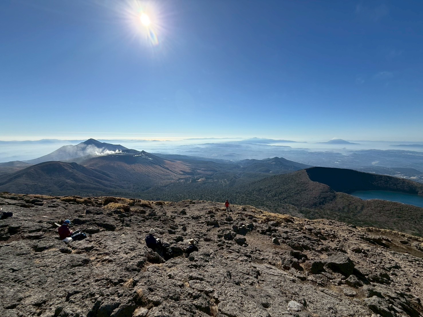 無事頂上に着きました。快晴で日差しが強い為、寒さもなく風がとても気持ち良いです。左奥の噴煙が上がっている山が新燃岳、右の大きな池が大浪池になります。